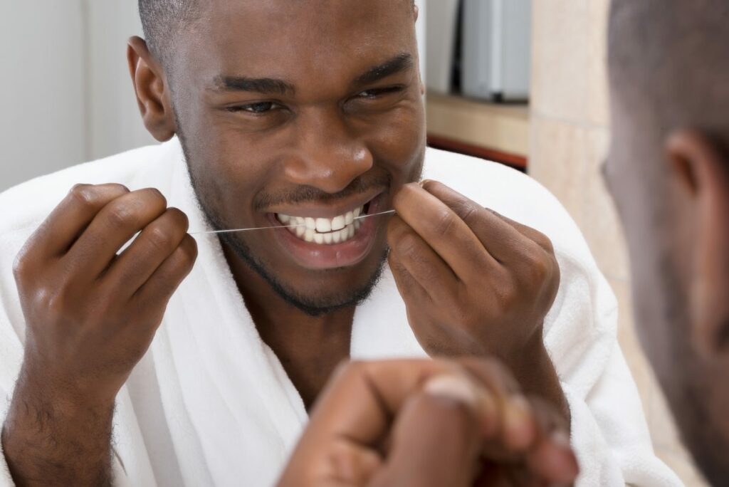 happy black man flossing teeth using dental floss